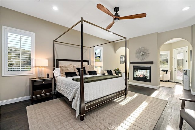 bedroom featuring recessed lighting, arched walkways, wood finished floors, and a multi sided fireplace