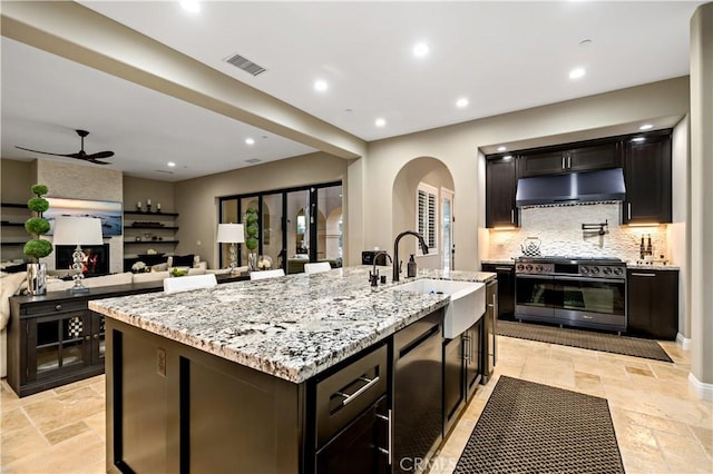 kitchen with stainless steel range, a center island with sink, stone tile floors, open floor plan, and under cabinet range hood