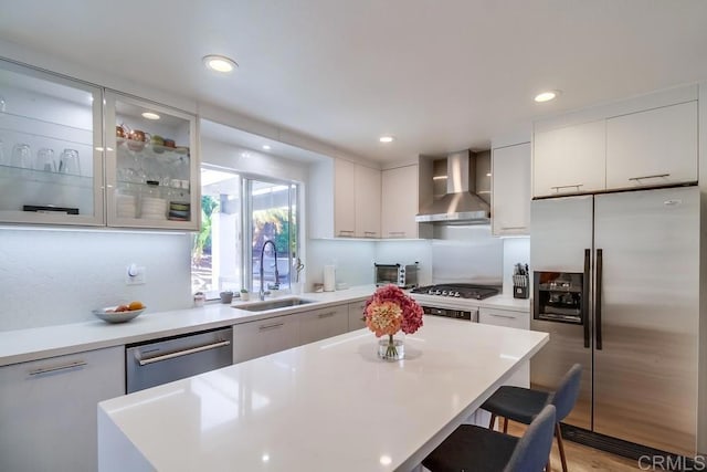 kitchen featuring white cabinetry, sink, a breakfast bar area, stainless steel appliances, and wall chimney range hood