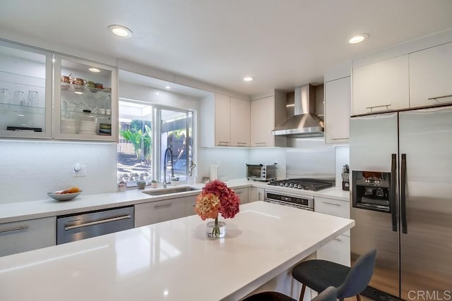 kitchen featuring sink, a breakfast bar area, white cabinets, stainless steel appliances, and wall chimney exhaust hood