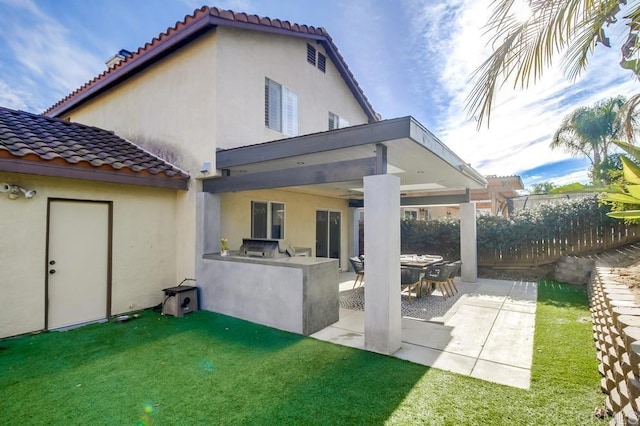 back of house featuring a bar, an outdoor kitchen, a yard, and a patio