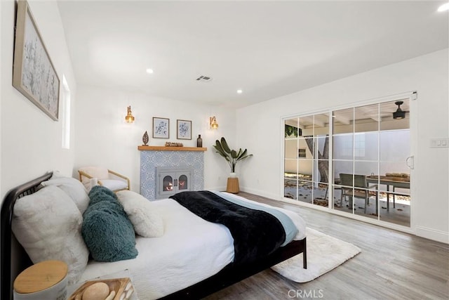 bedroom featuring access to exterior, hardwood / wood-style flooring, and a tile fireplace