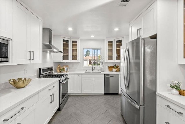 kitchen featuring wall chimney range hood, sink, appliances with stainless steel finishes, light stone counters, and white cabinets