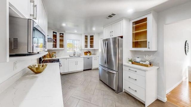 kitchen with white cabinetry, sink, light stone counters, and appliances with stainless steel finishes