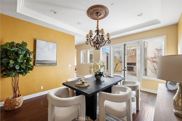 dining room with dark wood-type flooring, a tray ceiling, and crown molding