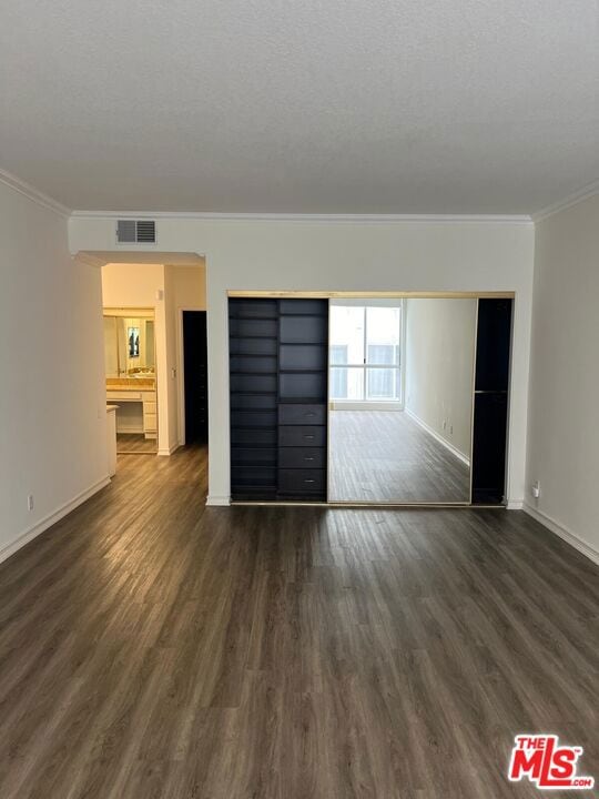 empty room featuring dark wood-type flooring, crown molding, and a textured ceiling