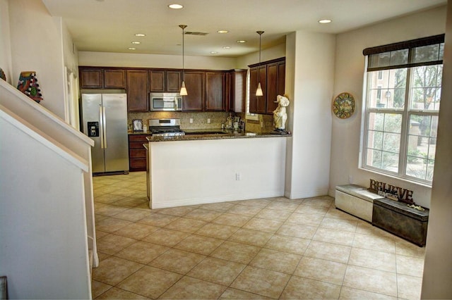 kitchen featuring pendant lighting, a healthy amount of sunlight, dark stone countertops, and appliances with stainless steel finishes