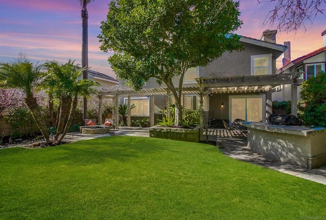 yard at dusk featuring an outdoor kitchen, an outdoor fire pit, a pergola, and a patio