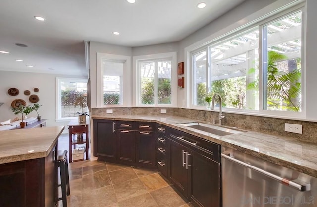 kitchen with stainless steel dishwasher, dark brown cabinetry, light stone countertops, and sink