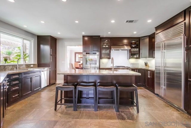 kitchen featuring light stone counters, appliances with stainless steel finishes, sink, and a kitchen island with sink