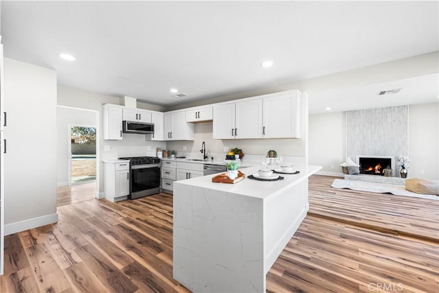 kitchen with sink, white cabinetry, appliances with stainless steel finishes, kitchen peninsula, and hardwood / wood-style flooring