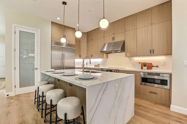 kitchen featuring light brown cabinetry, sink, decorative light fixtures, a center island with sink, and appliances with stainless steel finishes