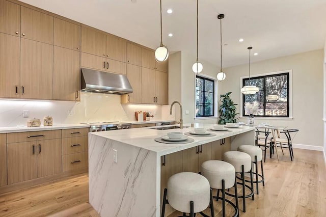 kitchen with sink, light hardwood / wood-style flooring, a kitchen island with sink, hanging light fixtures, and light brown cabinets