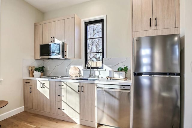 kitchen with sink, backsplash, stainless steel appliances, light brown cabinets, and light hardwood / wood-style flooring