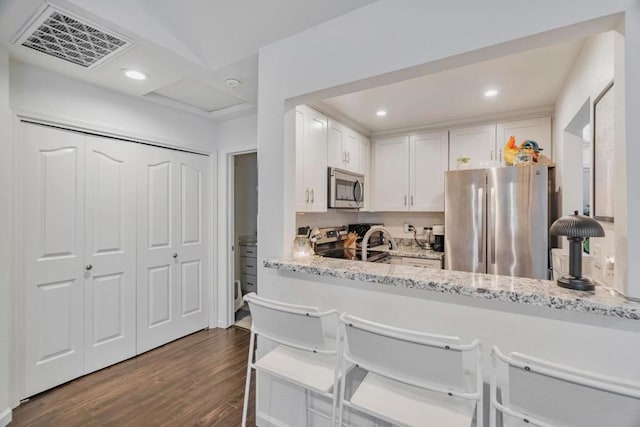 kitchen featuring a breakfast bar area, white cabinetry, appliances with stainless steel finishes, dark hardwood / wood-style flooring, and light stone countertops