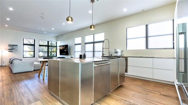 kitchen with decorative light fixtures, white cabinetry, an island with sink, dishwasher, and light wood-type flooring