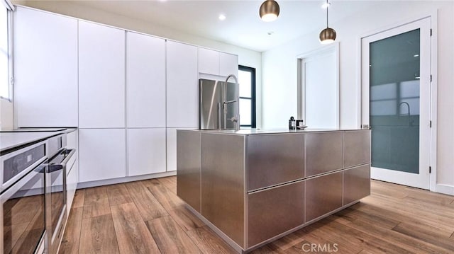 kitchen with decorative light fixtures, light wood-type flooring, a kitchen island, stainless steel appliances, and white cabinets