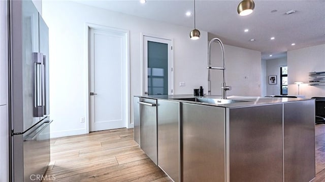 kitchen featuring sink, hanging light fixtures, appliances with stainless steel finishes, a kitchen island with sink, and light hardwood / wood-style floors