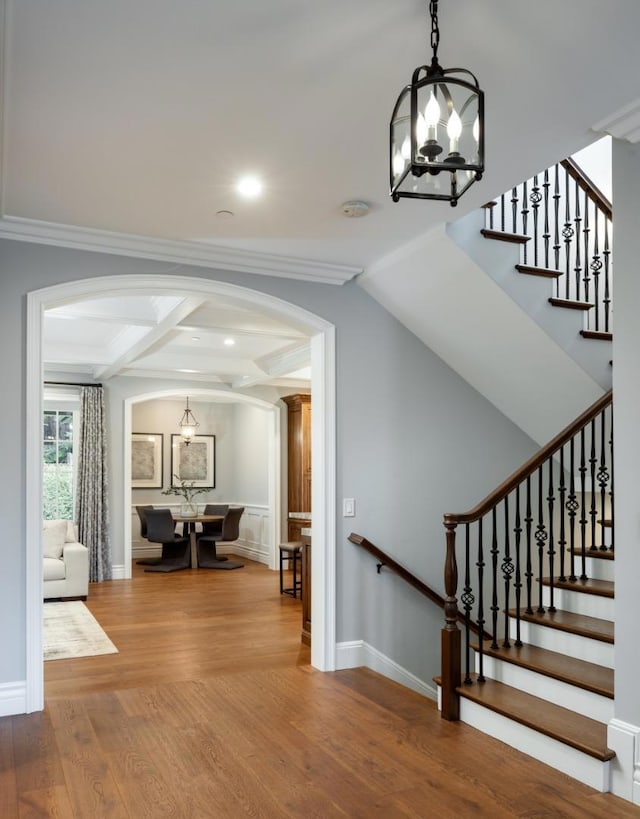 staircase with hardwood / wood-style flooring, crown molding, an inviting chandelier, coffered ceiling, and beamed ceiling