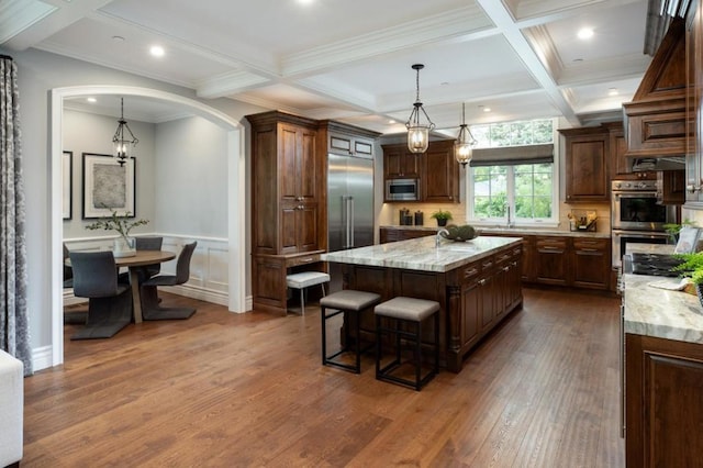 kitchen with dark hardwood / wood-style floors, decorative light fixtures, built in appliances, light stone counters, and a spacious island