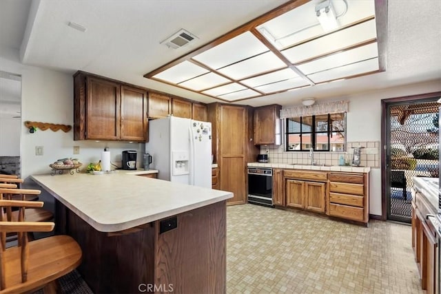 kitchen with black dishwasher, sink, a kitchen bar, white fridge with ice dispenser, and kitchen peninsula