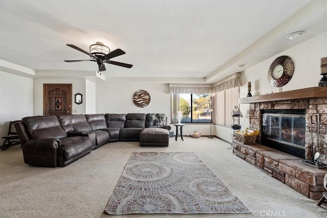 living room with a stone fireplace, carpet, and ceiling fan