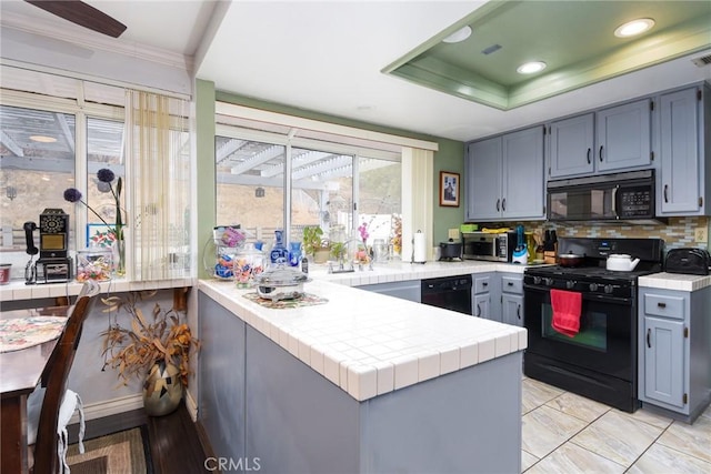 kitchen with tile counters, decorative backsplash, a peninsula, black appliances, and a raised ceiling