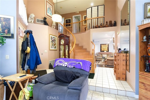 living area with light tile patterned flooring, visible vents, stairs, and a towering ceiling