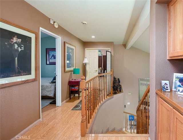 hallway with vaulted ceiling with beams, an upstairs landing, baseboards, and light wood finished floors