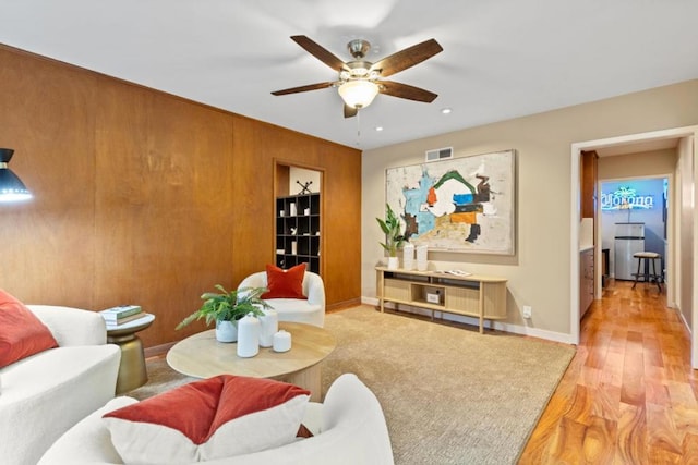 living room with ceiling fan, light hardwood / wood-style floors, and wood walls