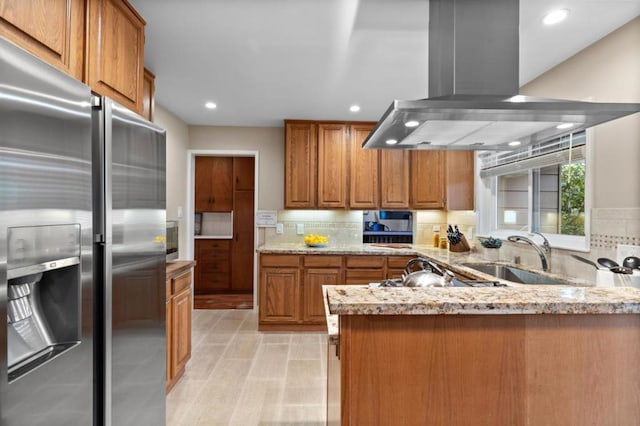 kitchen featuring sink, stainless steel fridge with ice dispenser, kitchen peninsula, island exhaust hood, and light stone countertops