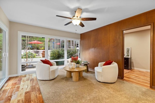 living room with ceiling fan, light hardwood / wood-style floors, and wood walls