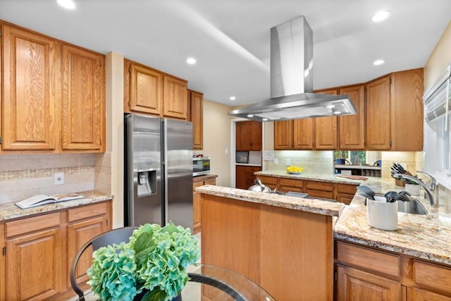 kitchen with sink, light stone counters, tasteful backsplash, island range hood, and stainless steel appliances