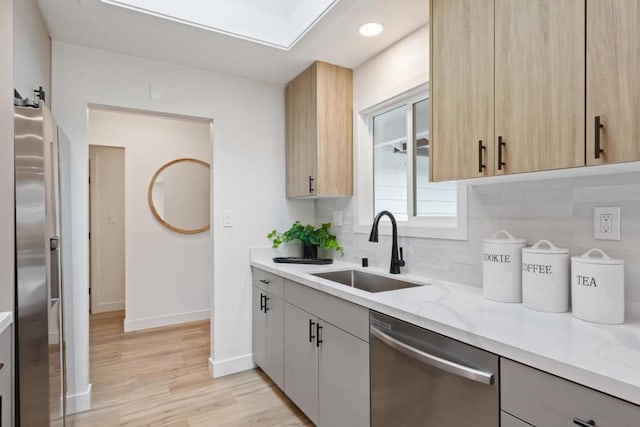 kitchen with light brown cabinetry, sink, appliances with stainless steel finishes, light stone countertops, and backsplash