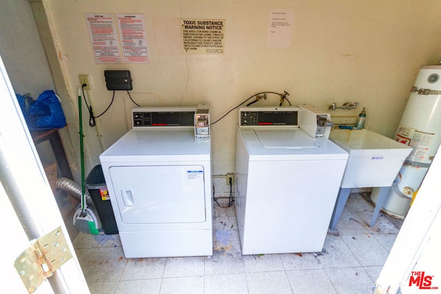 laundry area with strapped water heater, light tile patterned floors, and washer and clothes dryer