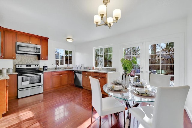 kitchen featuring sink, hanging light fixtures, hardwood / wood-style floors, stainless steel appliances, and light stone countertops