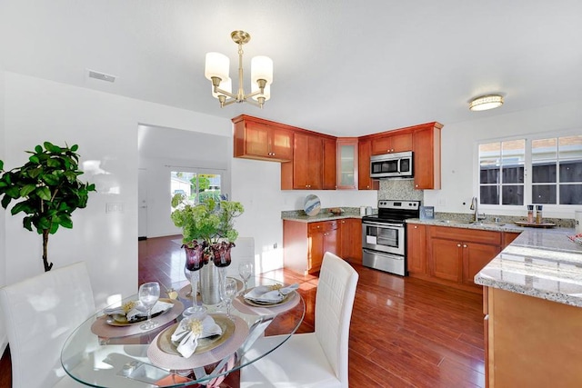 kitchen featuring dark wood-type flooring, sink, hanging light fixtures, stainless steel appliances, and light stone countertops