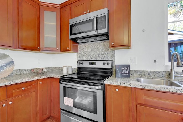 kitchen with tasteful backsplash, stainless steel appliances, light stone countertops, and sink