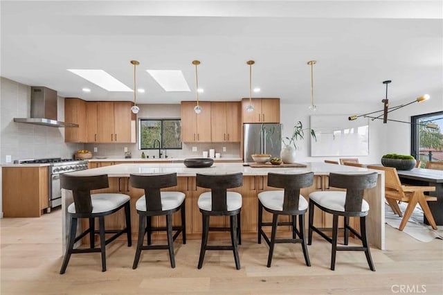 kitchen featuring a spacious island, wall chimney exhaust hood, sink, pendant lighting, and stainless steel appliances