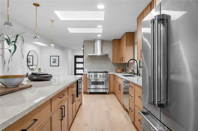 kitchen with a skylight, sink, premium appliances, hanging light fixtures, and wall chimney exhaust hood