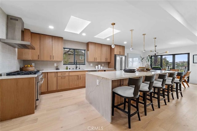 kitchen with wall chimney range hood, premium appliances, decorative light fixtures, and a center island