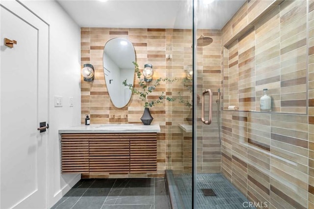 bathroom with a shower with door, vanity, tile patterned flooring, and backsplash