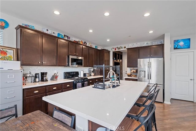 kitchen featuring sink, a breakfast bar, a kitchen island with sink, dark brown cabinets, and stainless steel appliances