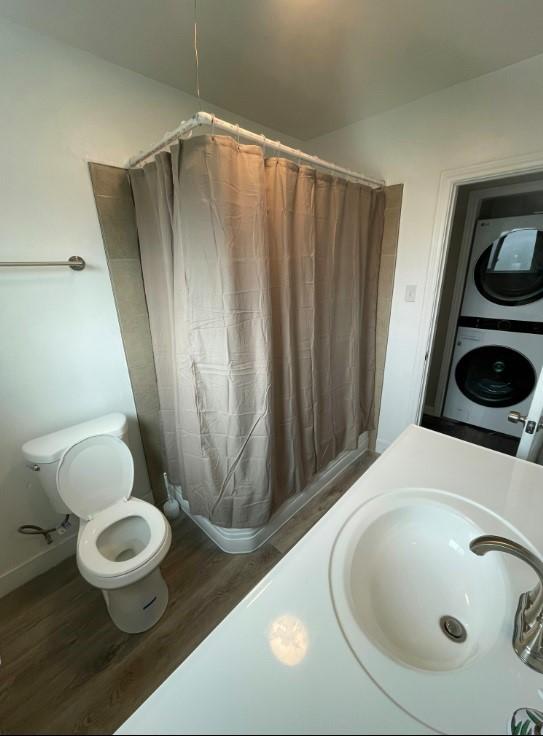 bathroom with sink, hardwood / wood-style flooring, stacked washing maching and dryer, toilet, and walk in shower