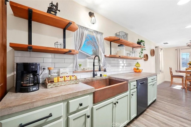 kitchen featuring sink, light wood-type flooring, dishwasher, green cabinets, and decorative backsplash