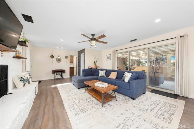 living room featuring a stone fireplace, hardwood / wood-style floors, and ceiling fan