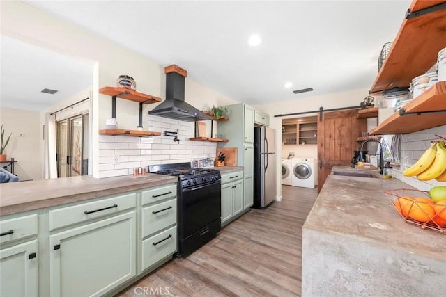 kitchen featuring sink, stainless steel fridge, exhaust hood, a barn door, and black gas range