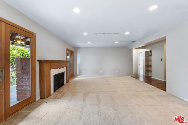 unfurnished living room with light colored carpet, a fireplace, and track lighting