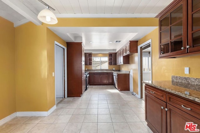 kitchen featuring decorative light fixtures, light tile patterned floors, beam ceiling, and stone counters