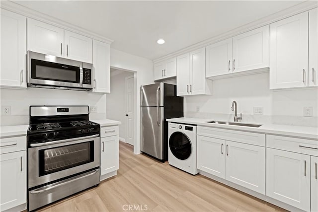 kitchen featuring sink, stainless steel appliances, light hardwood / wood-style floors, white cabinets, and washer / dryer